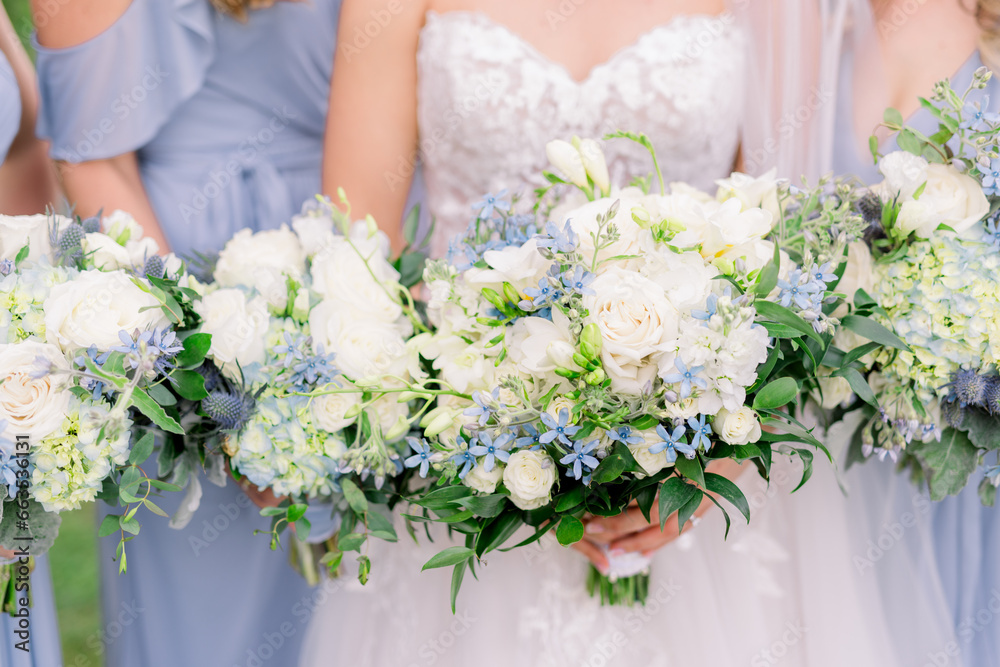 A bride and bridesmaids in blue dresses holds a white bouquet with blue flowers. A bride and bridesmaids in blue dresses holds a white bouquet with blue flowers.