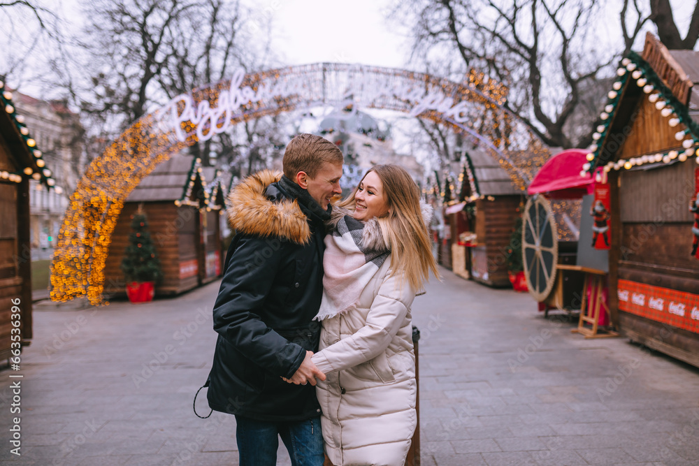 Attractive couple in love. Handsome man and his pretty girlfriend are holding hands while enjoying spending time together while standing at the winter christmas market.