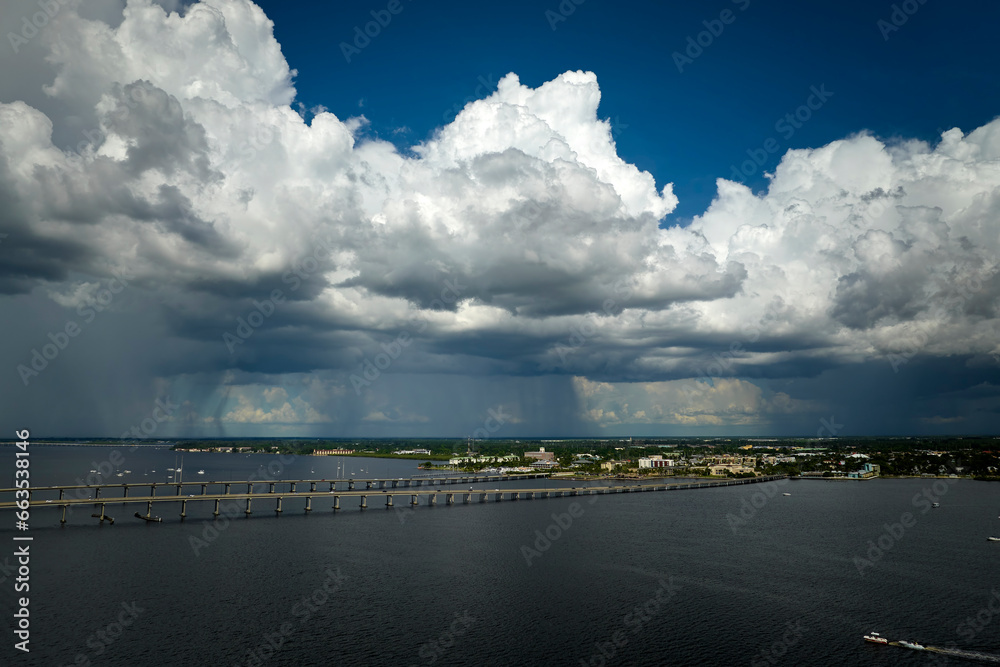 Fototapeta premium Stormy clouds forming from evaporating humidity of ocean water before thunderstorm over traffic bridge connecting Punta Gorda and Port Charlotte over Peace River. Bad weather conditions for driving