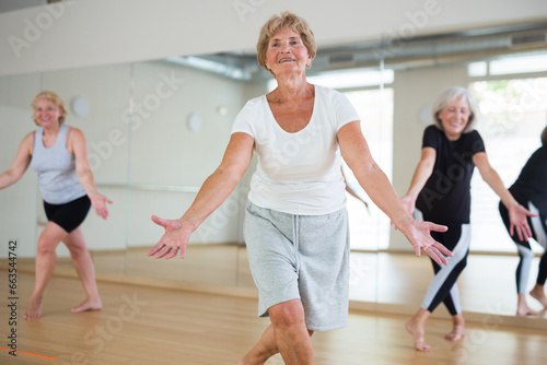 Portrait of cheerful senior woman enjoying active dancing during group training in dance studio.