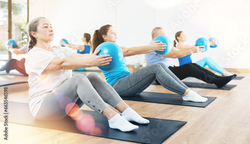 Class of male and women of different ages in active wear pressing balls in hands exercise during Pilates training together in gym