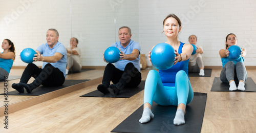 Group of young elderly people in sportswear exercising Pilates with mini balls while lying on mats in rehabilitation center