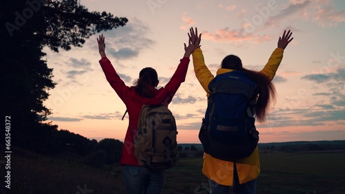 Women tourists with backpacks travel in forest, raise their hands enjoy sunset sky. Slow motion. Working as team of two friends, young female travelers adventures on vacation. People resting in nature