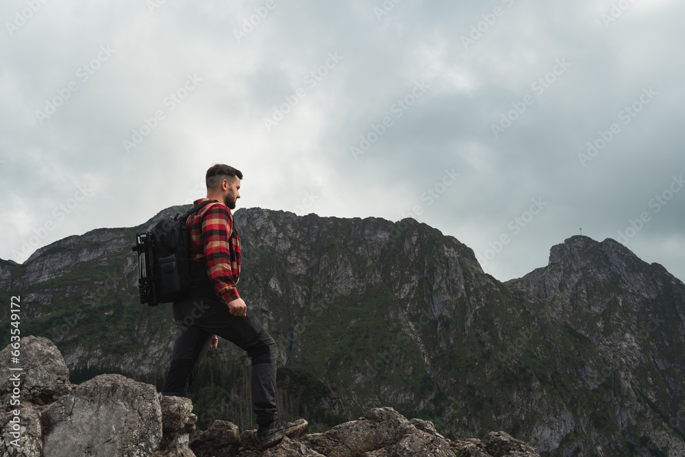 A male traveler photographer landscape painter in the Polish Tatra Mountains with a briefcase on his back walks to the Giewont rock in the evening, the sky is overcast.