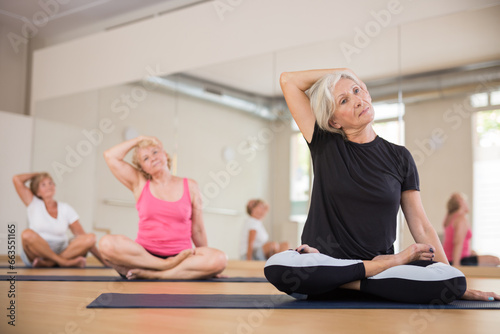 Group of mature women exercising while sitting on mats in lotus pose.