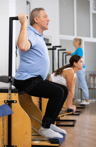 Focused mature man performing stretching exercises while using pilates Wanda chair machine in rehabilitation center
