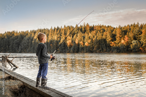 Little boy fishing on a lake surrounded by beautiful nature pine forest at sunrise 