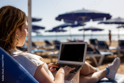 Relaxed woman enjoys beach vacation with laptop by the ocean. Nomadic Lifestyle Concept