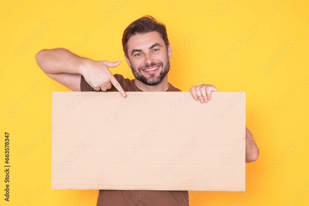 Happy man with blank banner isolated on studio background. Portrait of attractive man with empty blank poster. Man showing poster, pointing finger on signboard placard. Billboard or banner concept. Happy man with blank banner isolated on studio background. Portrait of attractive man with empty blank poster. Man showing poster, pointing finger on signboard placard. Billboard or banner concept.