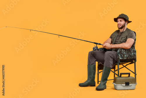 Fisherman with rod and tackle box on chair against yellow background