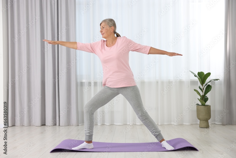Senior woman practicing yoga on mat at home