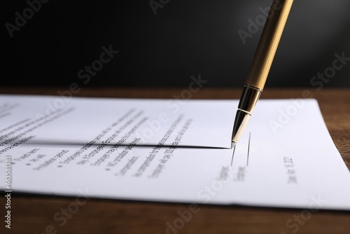 Signing document with pen on wooden table, closeup