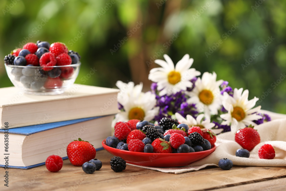 Different fresh ripe berries, beautiful flowers and books on wooden table outdoors Different fresh ripe berries, beautiful flowers and books on wooden table outdoors