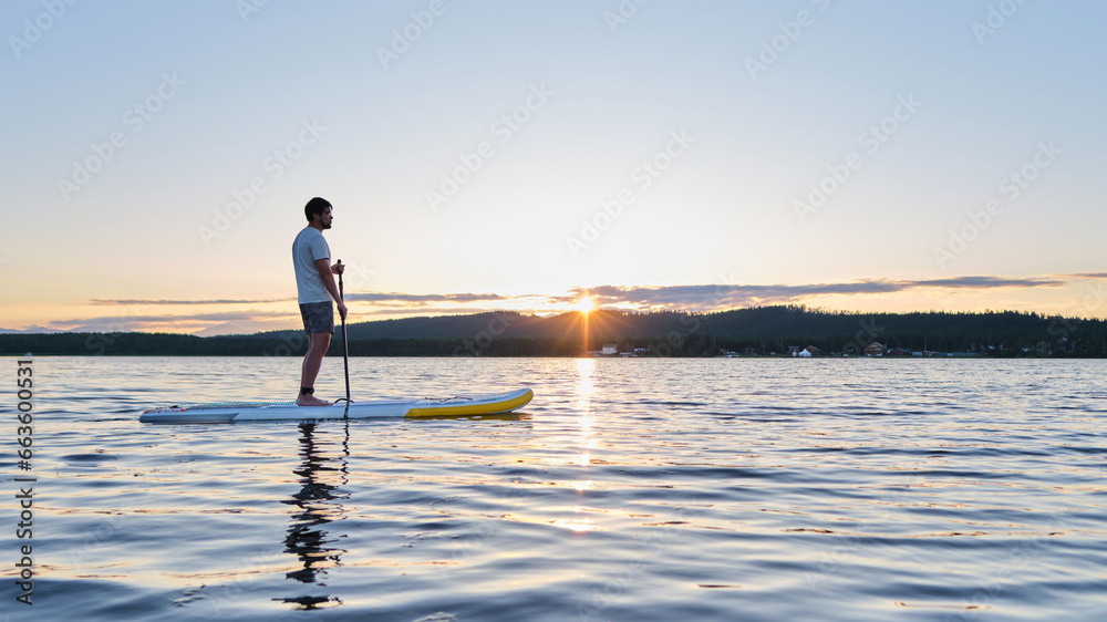 A man on a paddle board in the rays of sun.