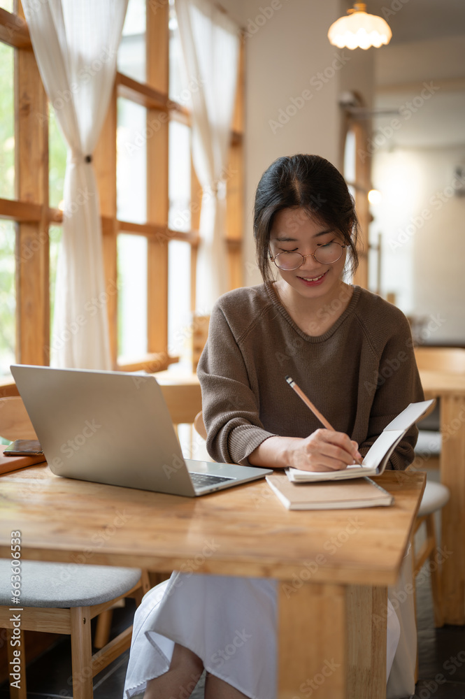 A woman is working remotely at a coffee shop, taking notes in her book and working on her laptop. A woman is working remotely at a coffee shop, taking notes in her book and working on her laptop.