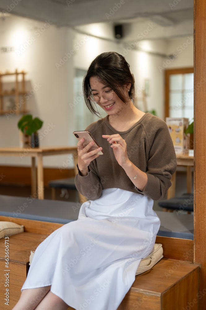 A beautiful woman is responding to messages through her smartphone while relaxing in a cosy cafe.