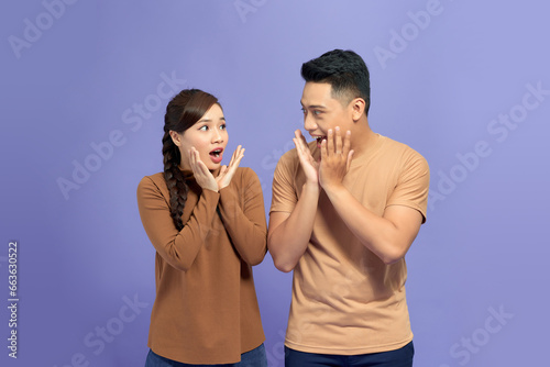 Cheerful young Asian couple being excited with fabulous secret isolated on violet background
