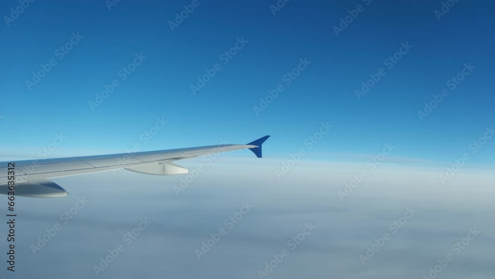 Wing of flying above clouds airplane as seen by passenger through porthole. Wide shot footage Wing of flying above clouds airplane as seen by passenger through porthole. Wide shot footage