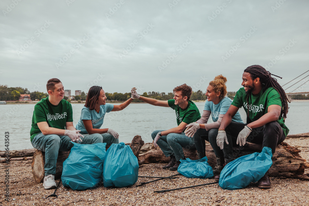 Five volunteers in uniforms sitting by the river doing a high five after collecting the waste