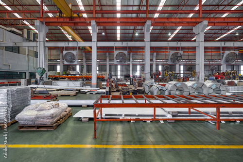 Metal sheets and steel sheet roll are placed on the floor in metal sheet factory. Large crane and truck are in the working area.