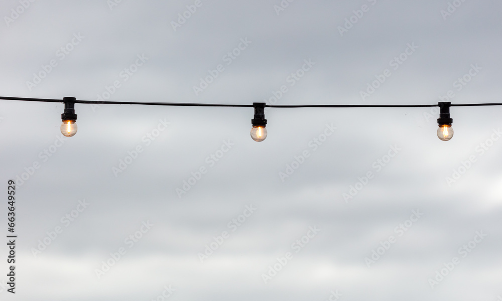Festive light bulbs shine against the background of the sky with clouds Festive light bulbs shine against the background of the sky with clouds