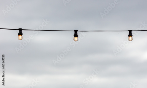 Festive light bulbs shine against the background of the sky with clouds © schankz