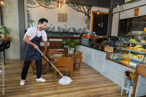 Konstfotografi Waiters handsome Indian wearing apron mopping the floor in cafe and bakery preparing to support customers come in restaurant