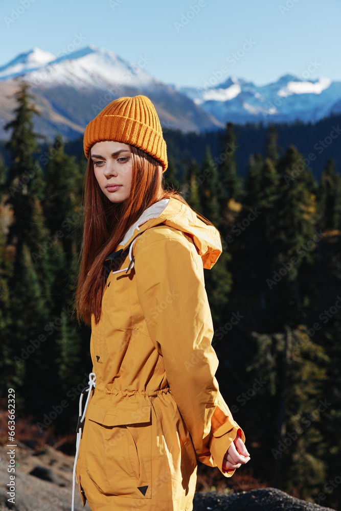 Woman in yellow raincoat hiking stands in front of mountains in yellow cap in autumn Woman in yellow raincoat hiking stands in front of mountains in yellow cap in autumn