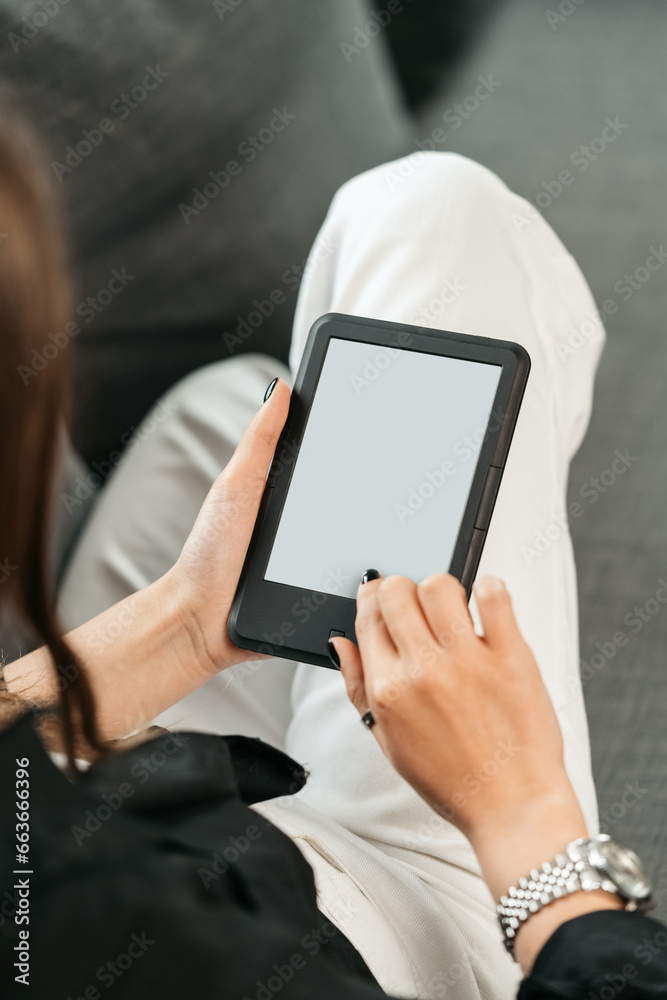 Young woman sitting the couch with an e-book