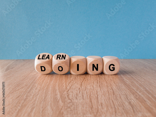 Learning by doing concept. Turned a cube and changes the word learning to doing, or vice versa. Beautiful wooden table blue background. Copy space.
