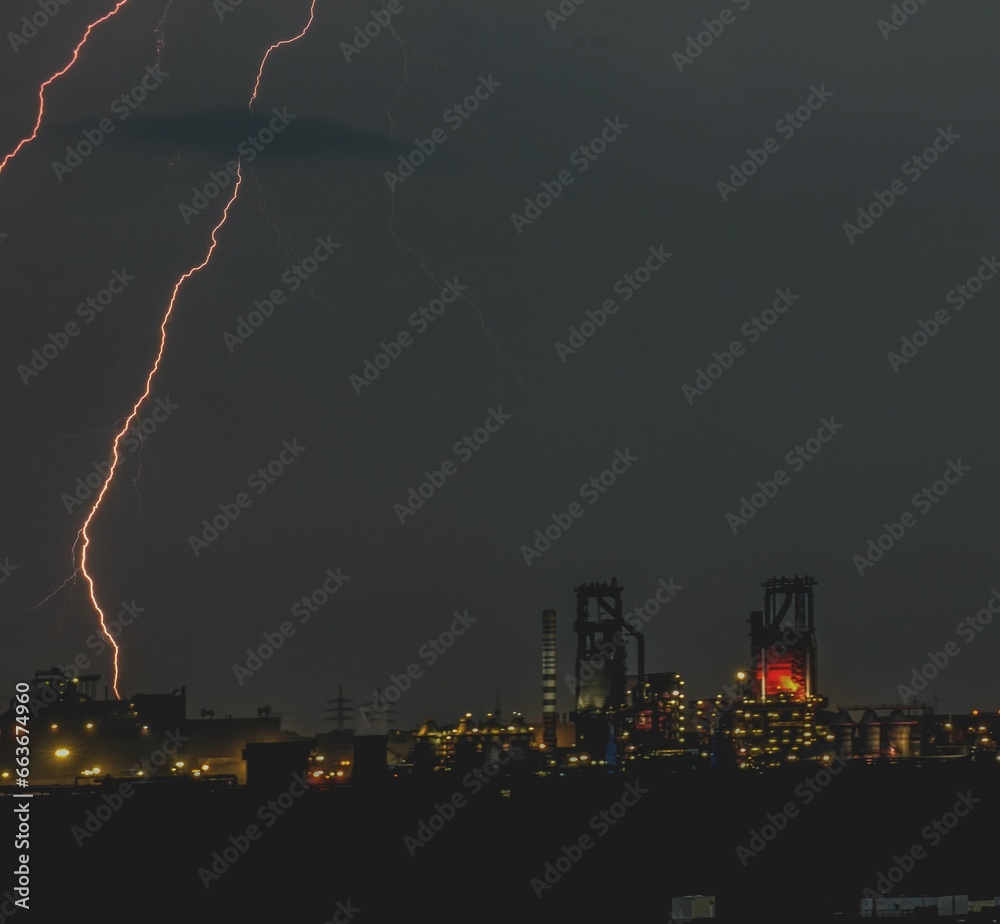 a lightning bolt hitting through the night sky above a refinery