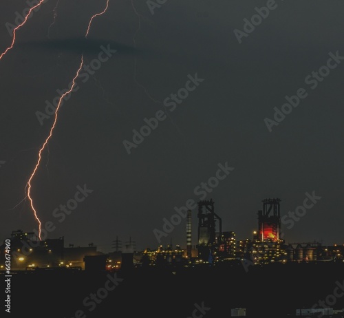 a lightning bolt hitting through the night sky above a refinery