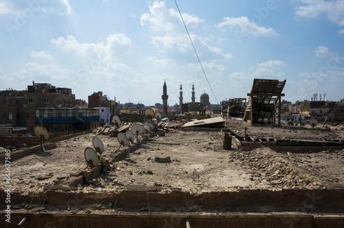 Roof in Islamic Cairo close up view with construction debris and many satellite dishes, Twin minarets and dome of Bab Zuweila on horizon, Egypt