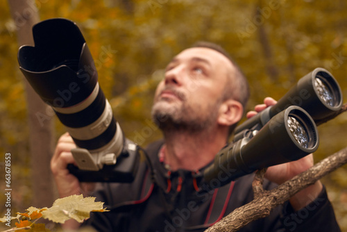 Man using binoculars and camera for birdwatching and other observing animals in nature.