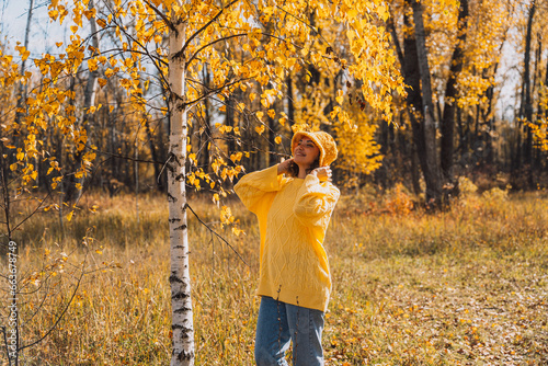 A lady in a yellow knitted sweater walks through the autumn forest. © Anastassiya 