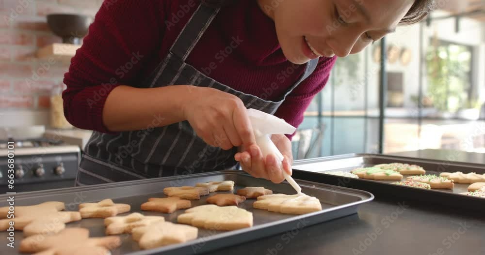 Happy biracial woman in apron decorating christmas cookies in kitchen, slow motion Happy biracial woman in apron decorating christmas cookies in kitchen, slow motion