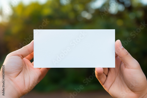 Close up of hands holding blank business card against blurred green foliage background