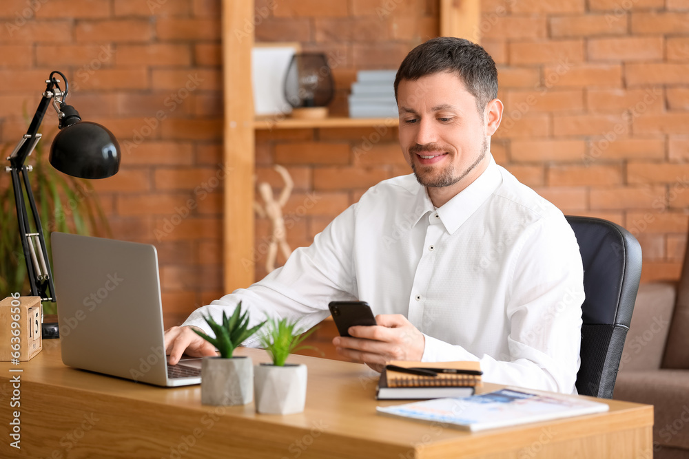 Businessman with smartphone and laptop at workplace in office