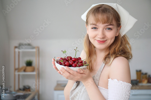 Beautiful happy young woman with bowl of cherries in kitchen