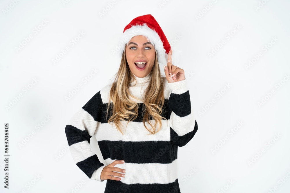 Beautiful hispanic woman wearing christmas hat and striped knitted sweater holding finger up having idea and posing