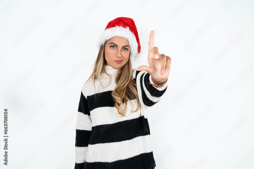 Beautiful hispanic woman wearing christmas hat and striped knitted sweater making fun of people with fingers on forehead doing loser gesture mocking and insulting. Beautiful hispanic woman wearing christmas hat and striped knitted sweater making fun of people with fingers on forehead doing loser gesture mocking and insulting.