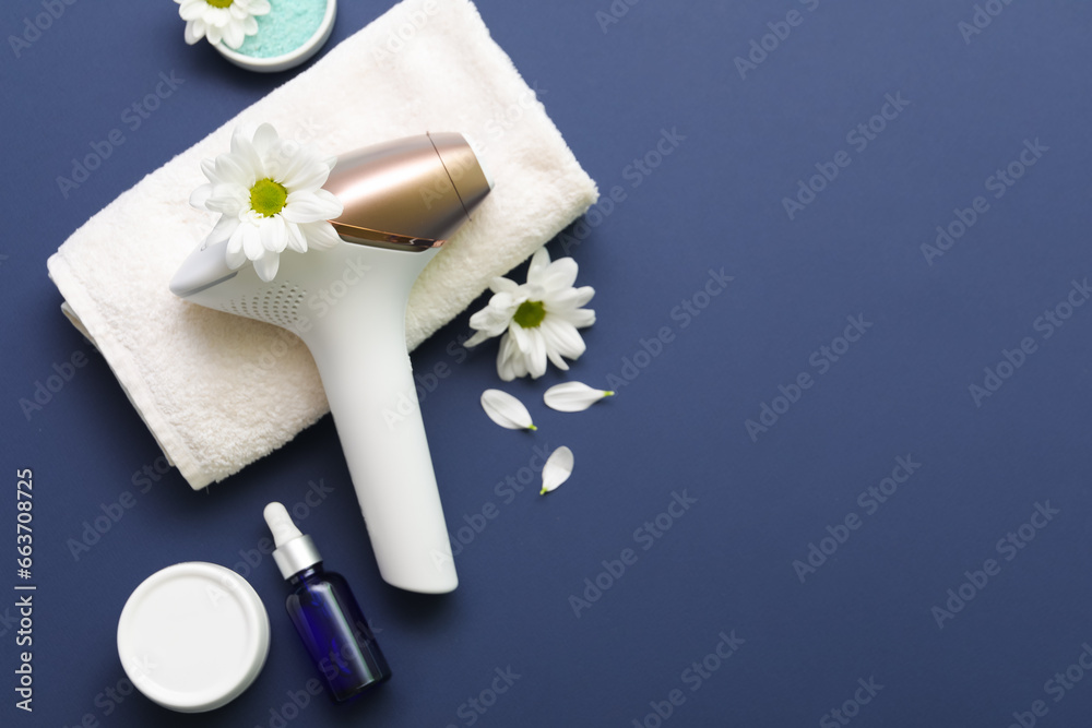 Modern photoepilator with beautiful flowers, bath towel and cosmetic products on dark blue background