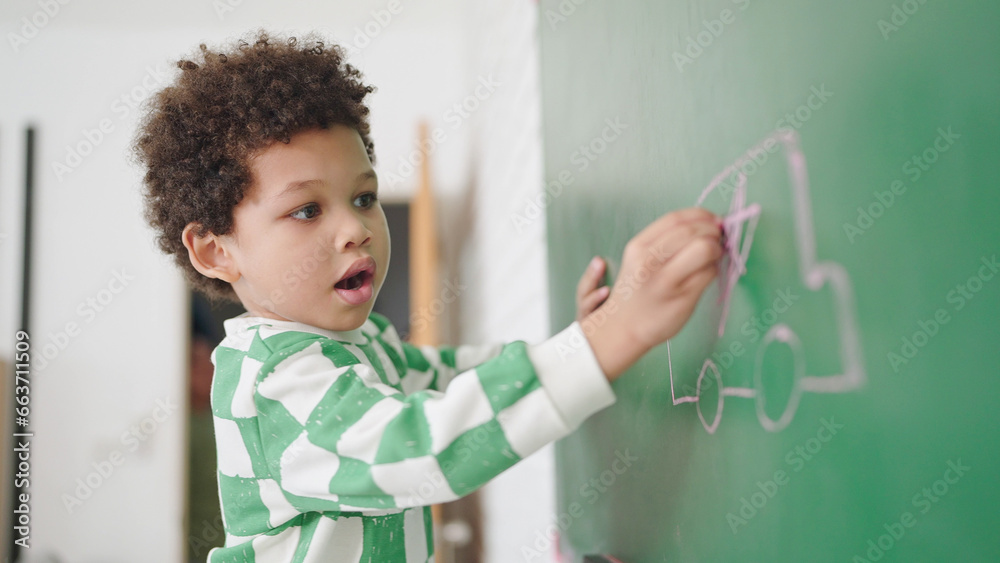 African american cute little child boy writes on a chalk board with chalk in classroom at school. Little boy writes on green board in classroom. Back to School. Education concept - obrazy, fototapety, plakaty 