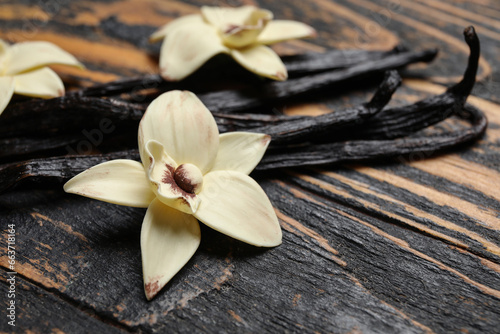 Aromatic vanilla sticks and flowers on black wooden background