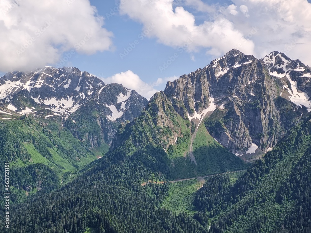 Fototapeta premium Snow-Capped Mountains with Green and Dry Grass, Clouds, and a Stunning Sky