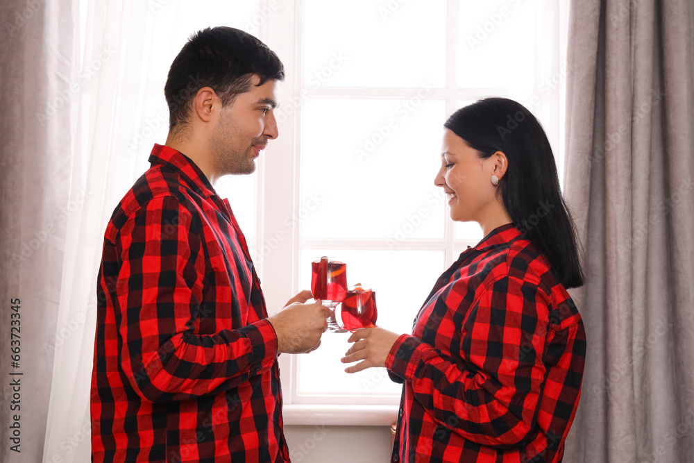 Young couple with glasses of mulled wine at home on Christmas eve Young couple with glasses of mulled wine at home on Christmas eve