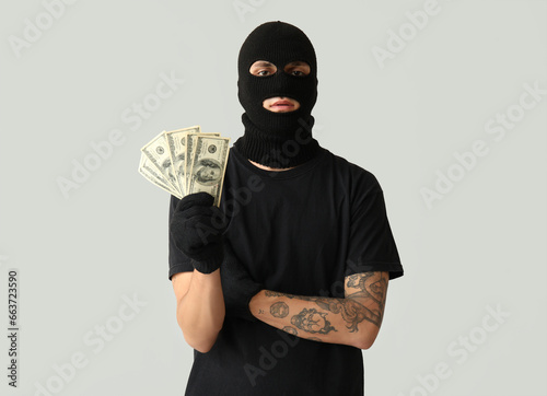 Male thief with dollar banknotes on grey background