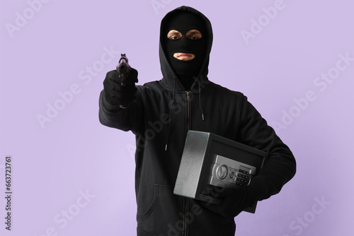 Fototapeta Naklejka Na Ścianę i Meble -  Male thief with gun and safe box on lilac background