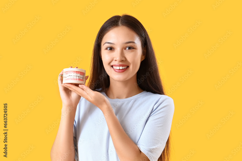 Smiling young Asian woman with jaw model on yellow background Smiling young Asian woman with jaw model on yellow background