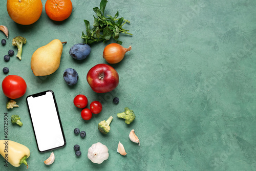 Fototapeta Naklejka Na Ścianę i Meble -  Mobile phone with fresh vegetables and fruits on green background. World Vegan Day concept
